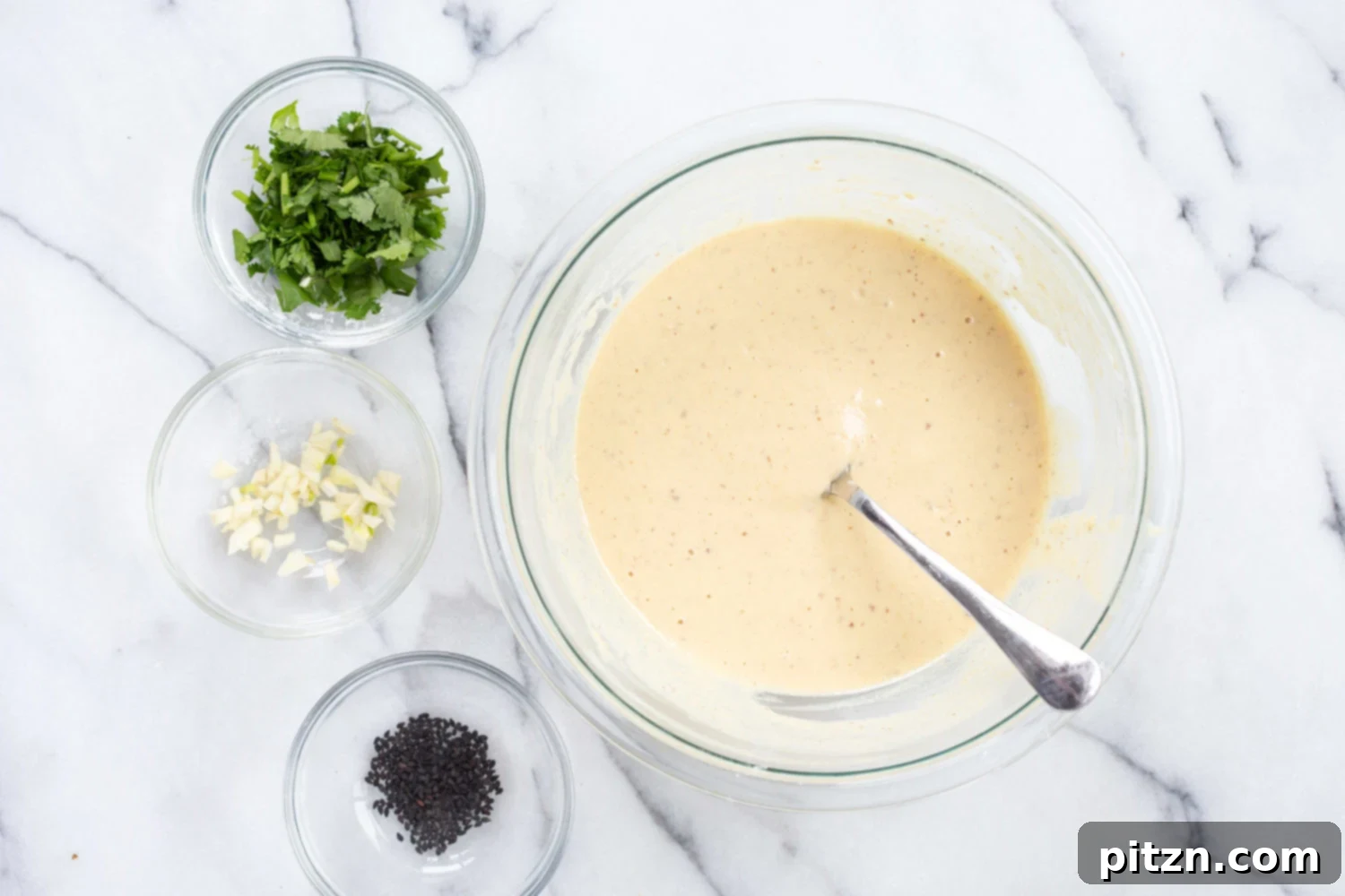 Naan batter in a bowl, with small bowls of various garnishes like seeds and fresh herbs, ready for topping