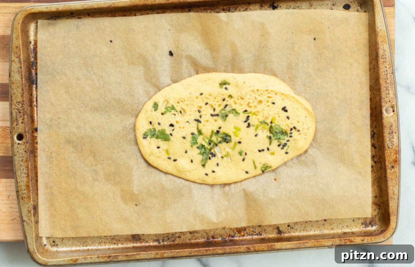 Partially baked Vegan Gluten Free Naan on a parchment-lined baking sheet, covered with another sheet of parchment for steaming