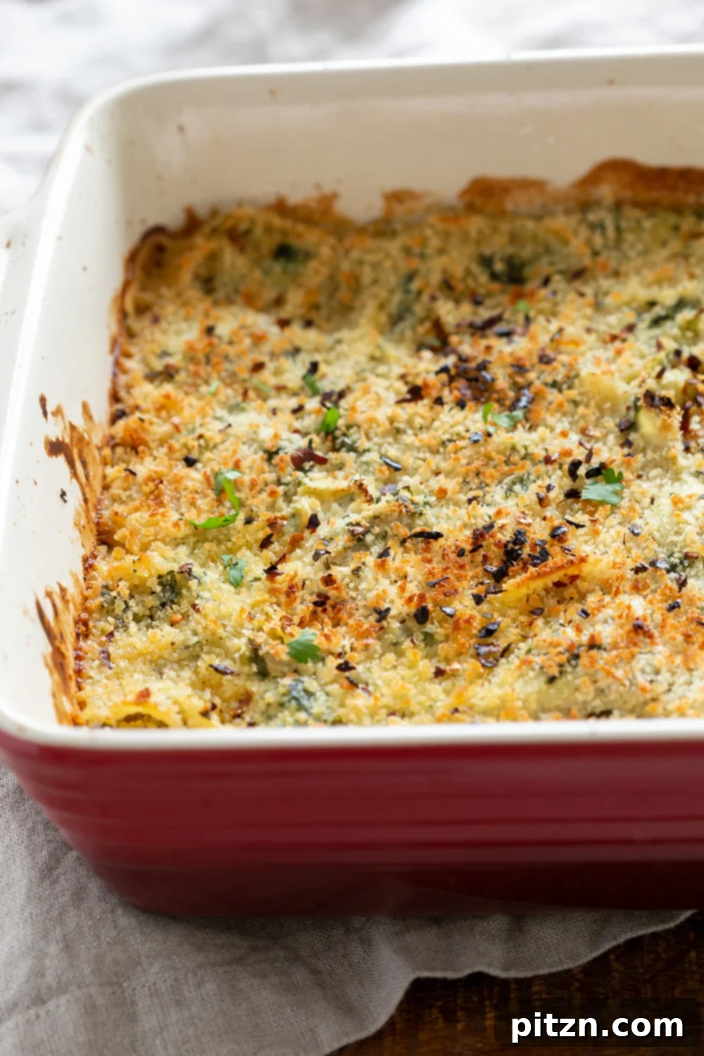 spinach pasta recipe side view close up of a red casserole dish with creamy vegan artichoke spinach pasta bake