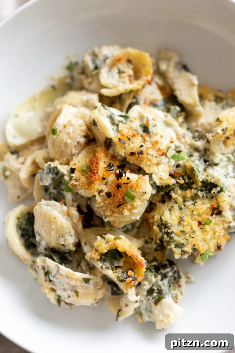 overhead shot of a plate of vegan spinach and artichoke pasta bake with breadcrumb topping