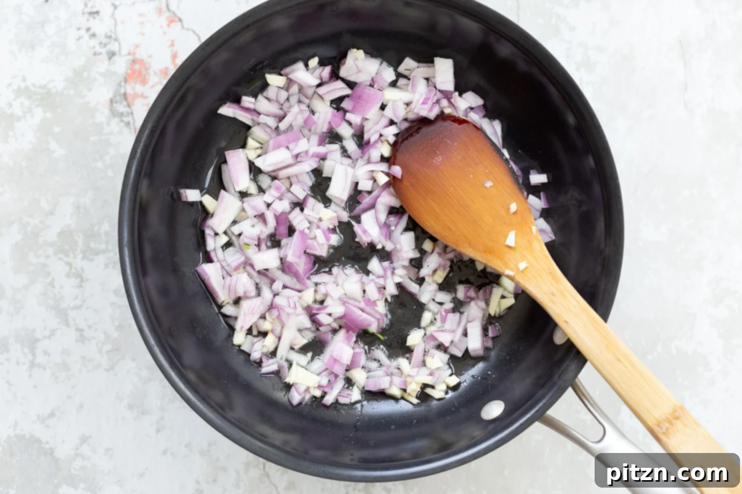 spinach pasta recipe chopped red onions being sauteed in a black skillet