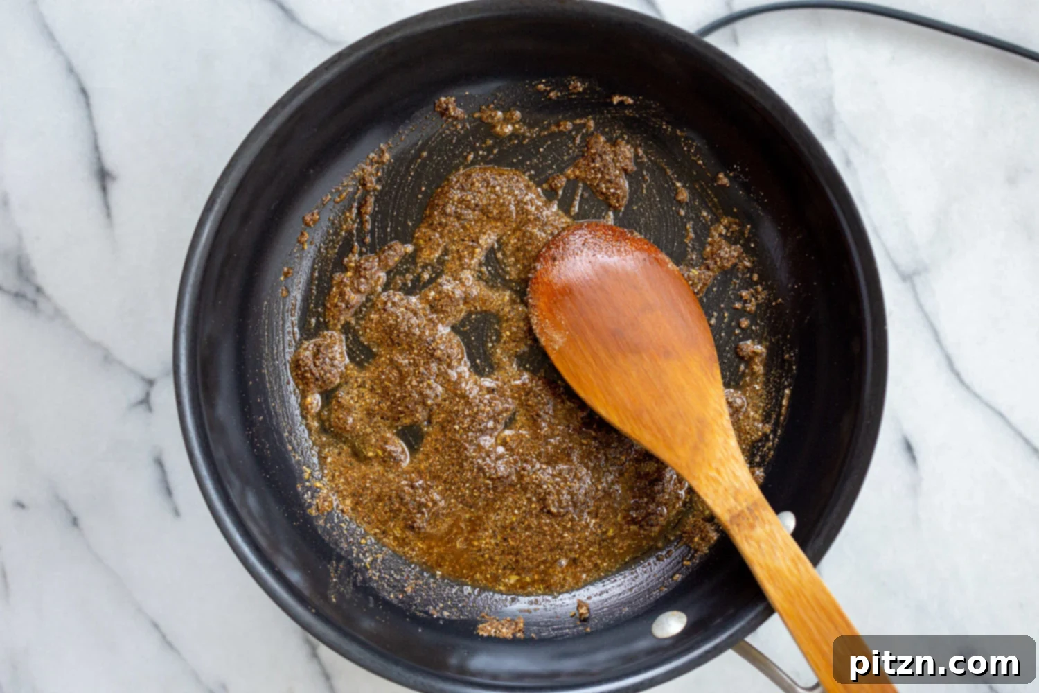 Ground and roasted spices sizzling in oil on a black skillet, creating an aromatic base for the Keema Madras.