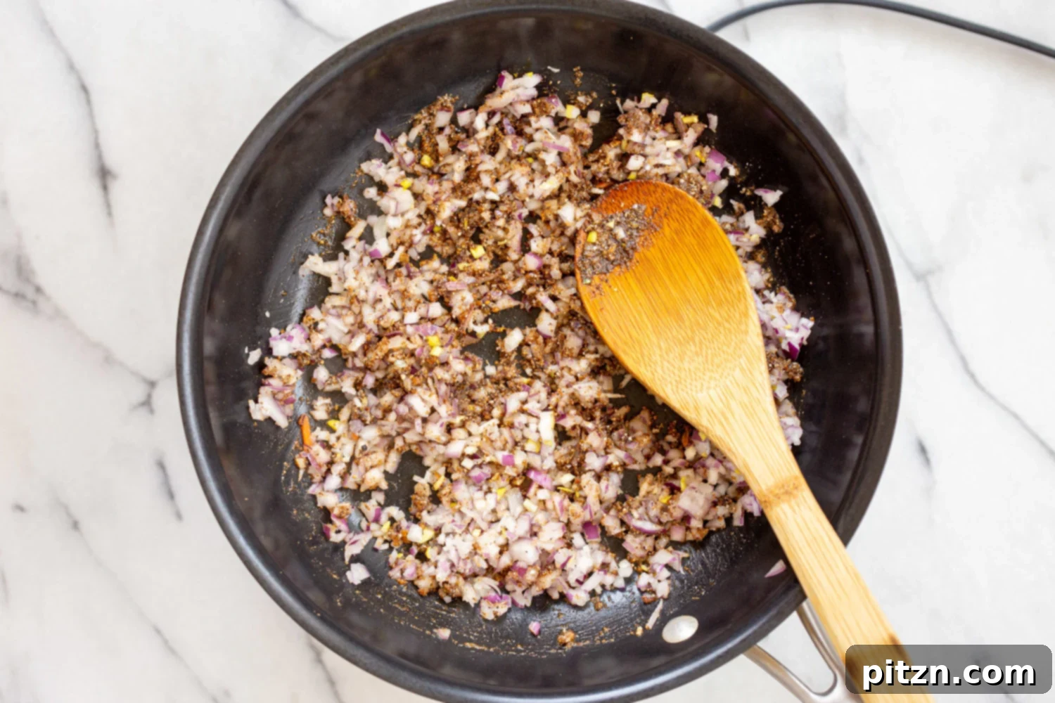 Sautéed onions and garlic mixed with roasted spices in a black skillet, releasing their sweet aroma.