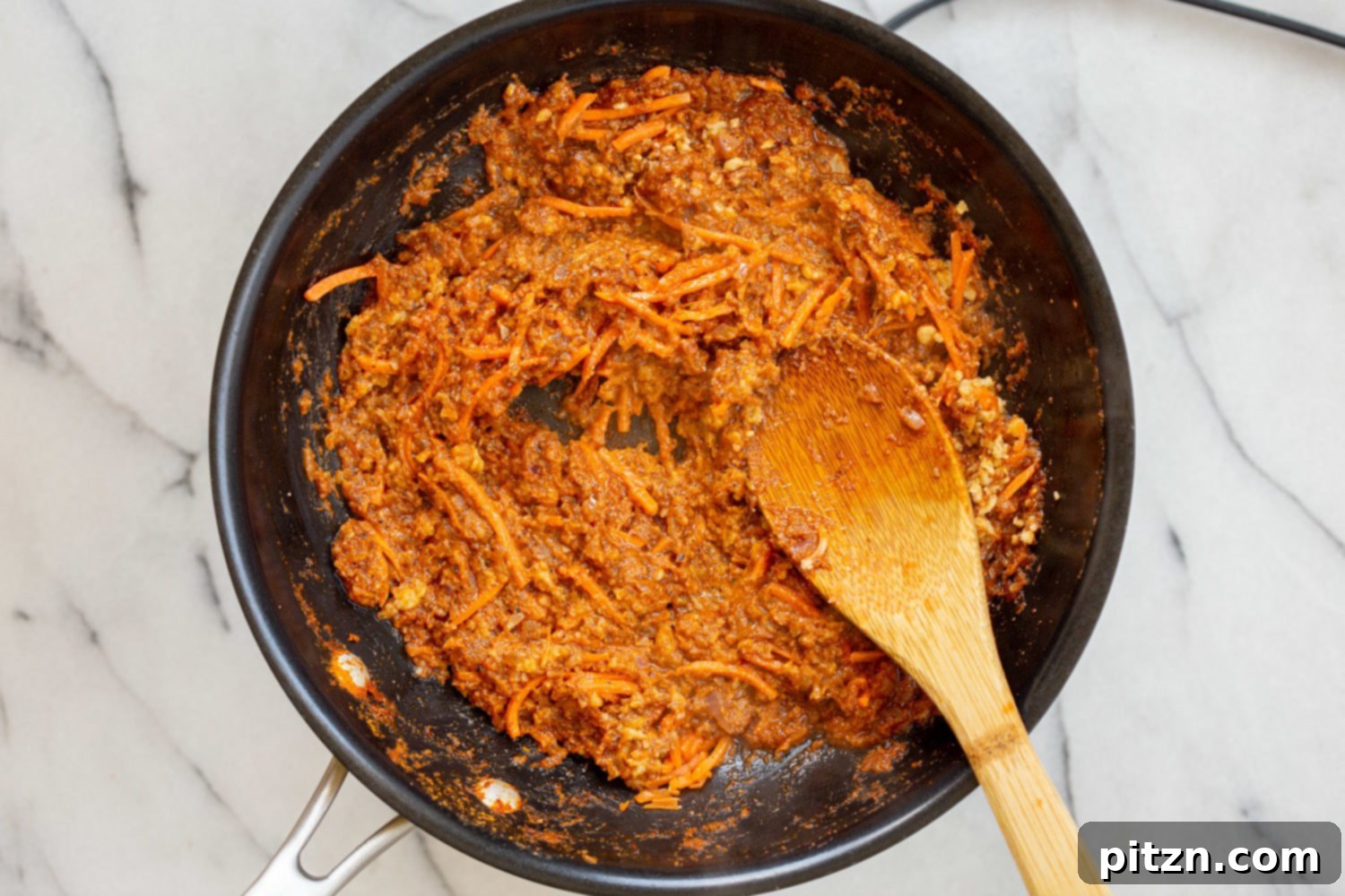 Carrots and crushed walnuts added to the simmering Keema Madras sauce in a black skillet, enhancing texture and flavor.