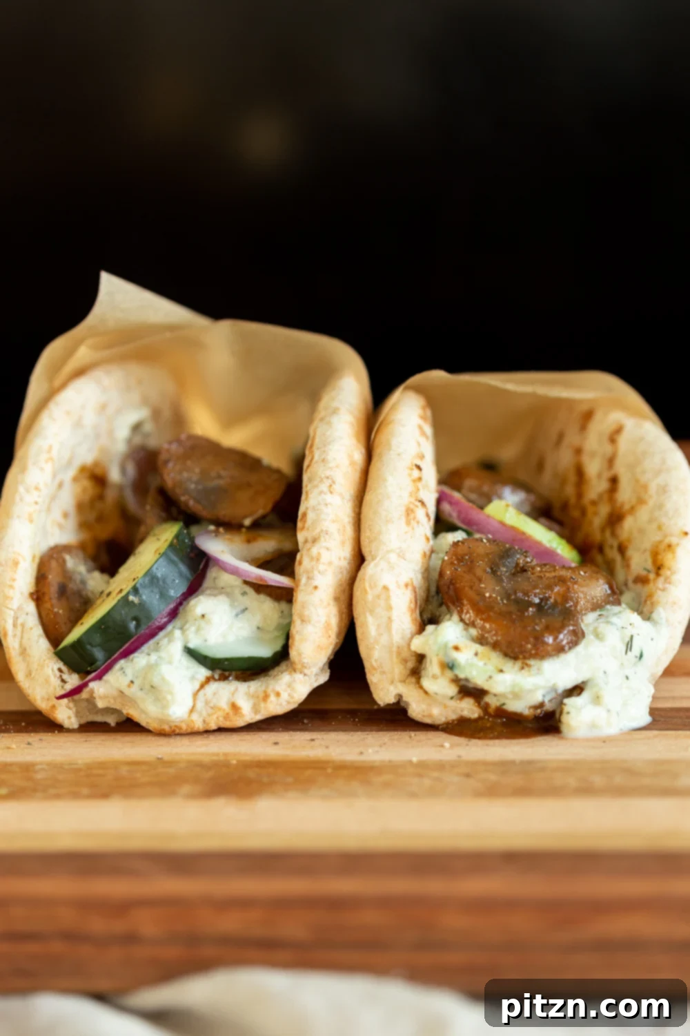 Two Vegan Gyros with mushrooms and a side of tzatziki artfully arranged on a wooden board, ready to be enjoyed.