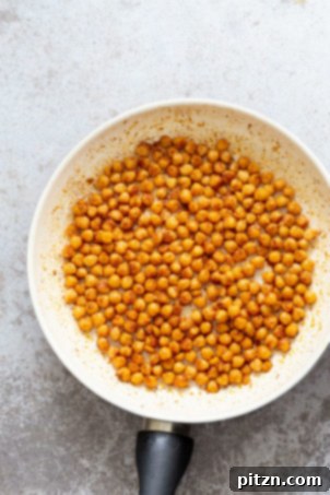 Shawarma Spiced Chickpeas sizzling in a white skillet, ready to top our Vegan Mediterranean Nachos.
