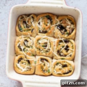 Ultimate Vegan Pesto Pizza Rolls 2 Overhead shot of freshly baked Vegan Pesto Pizza rolls, perfectly golden and arranged in a white casserole dish, garnished with fresh basil leaves.