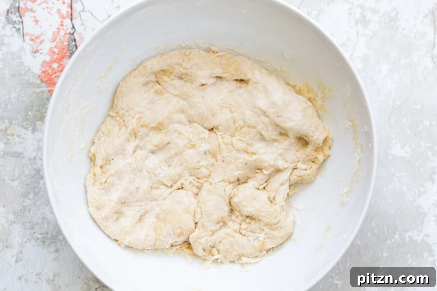 Pizza Dough Proofing Proofing pizza dough resting in a white bowl, covered with plastic wrap, showing its increased volume and readiness for the next step.