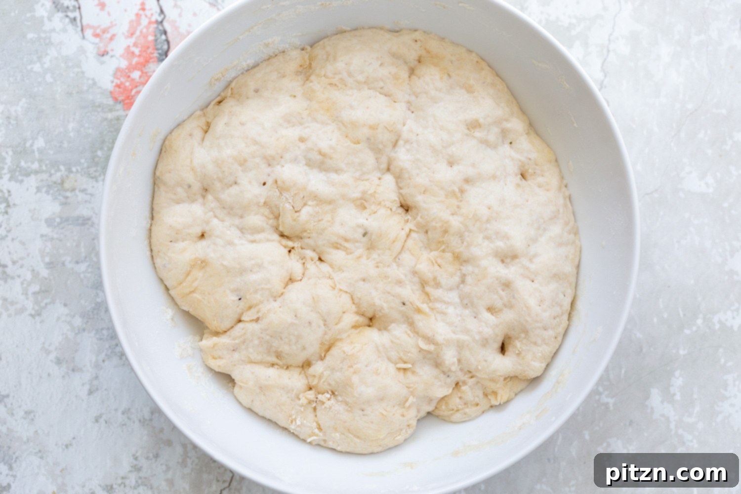 Risen Pizza Dough Fully proofed pizza dough, doubled in size and appearing fluffy, resting in a white bowl, ready to be punched down and rolled out.