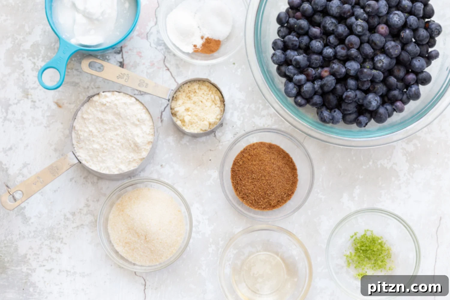 Various ingredients for Vegan Blueberry Cobbler laid out in bowls, including fresh blueberries, flour, and coconut milk.