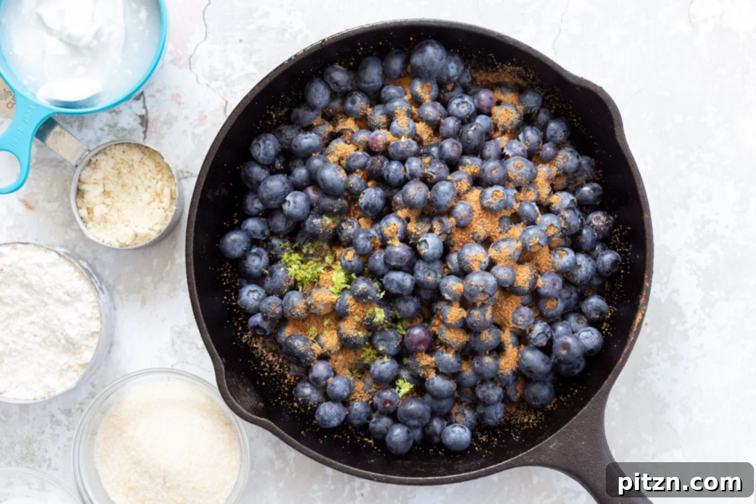 Fresh blueberries, sugar, and lemon zest mixed together in a cast iron skillet, ready for the cobbler topping.