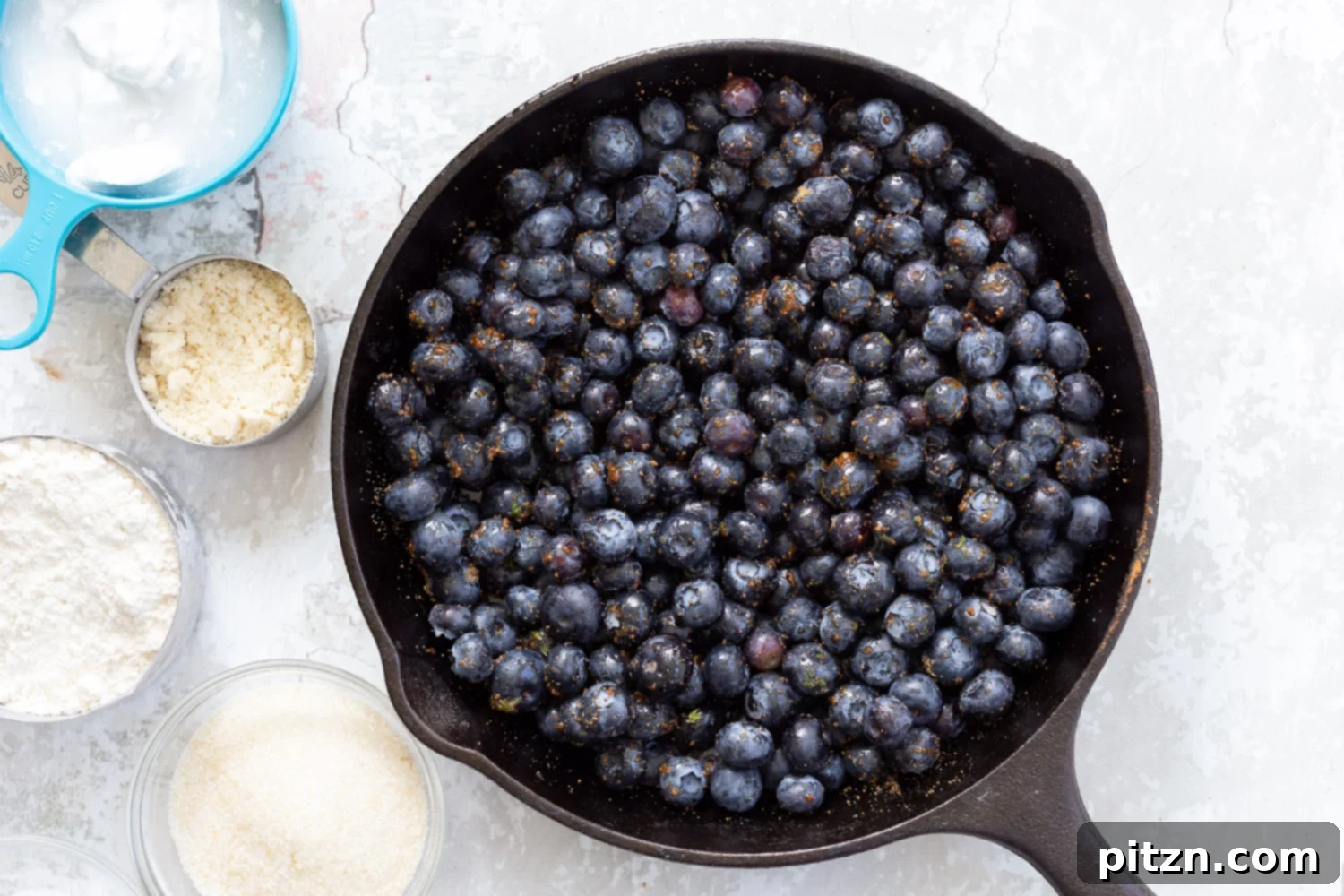Blueberries, sugar, and lemon zest fully combined in a cast iron skillet, forming the base of the Vegan Blueberry Cobbler.