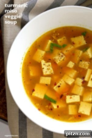 A bowl of comforting soup, possibly a hot and sour soup or miso soup, with visible tofu cubes and fresh herbs.