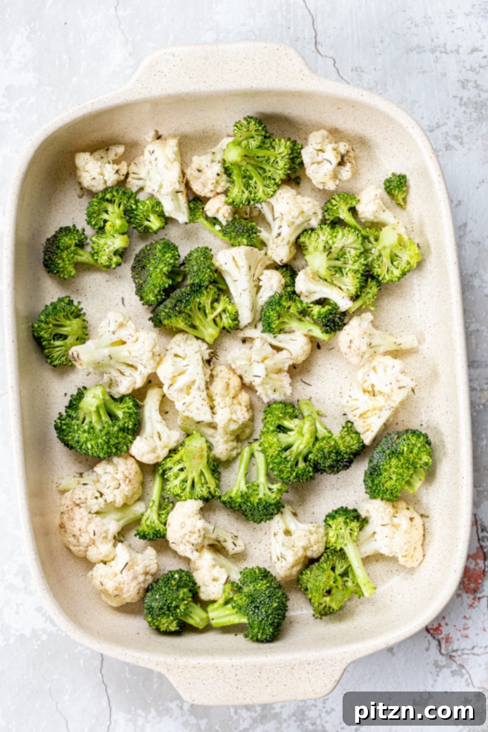 Veggies for our Roasted Broccoli Cauliflower Salad in a cream baking dish, ready for oven