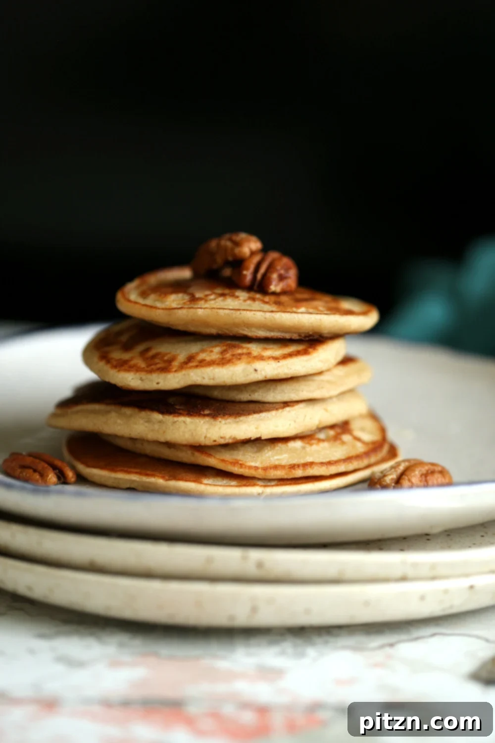 Stacked Vegan Banana Oat Pancakes on white plates, garnished with fresh berries and maple syrup, highlighting their fluffy texture.
