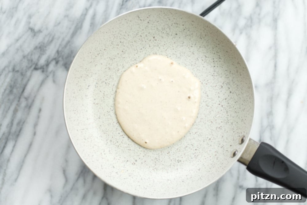 Banana Oat Pancake batter being poured onto a hot, white stone skillet, beginning to cook.