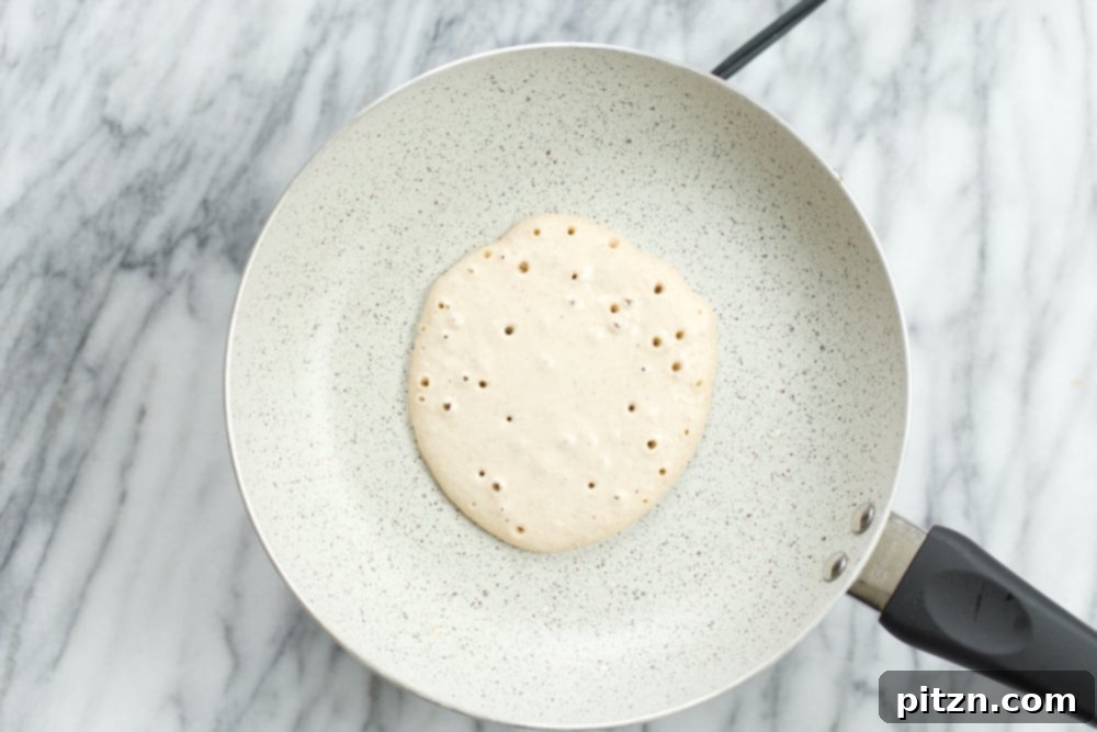 A Banana Oat Pancake cooking on a white stone skillet, showing golden-brown edges and a soft interior.