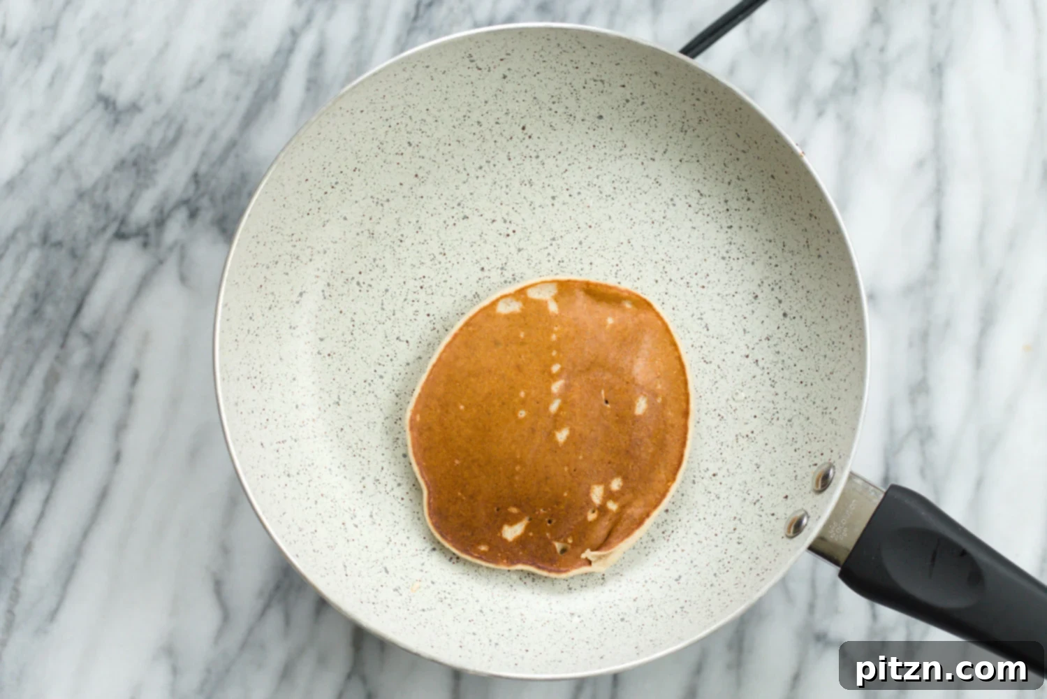 A freshly cooked Vegan Banana Oat Pancake being removed from a white stone skillet, ready to be stacked.