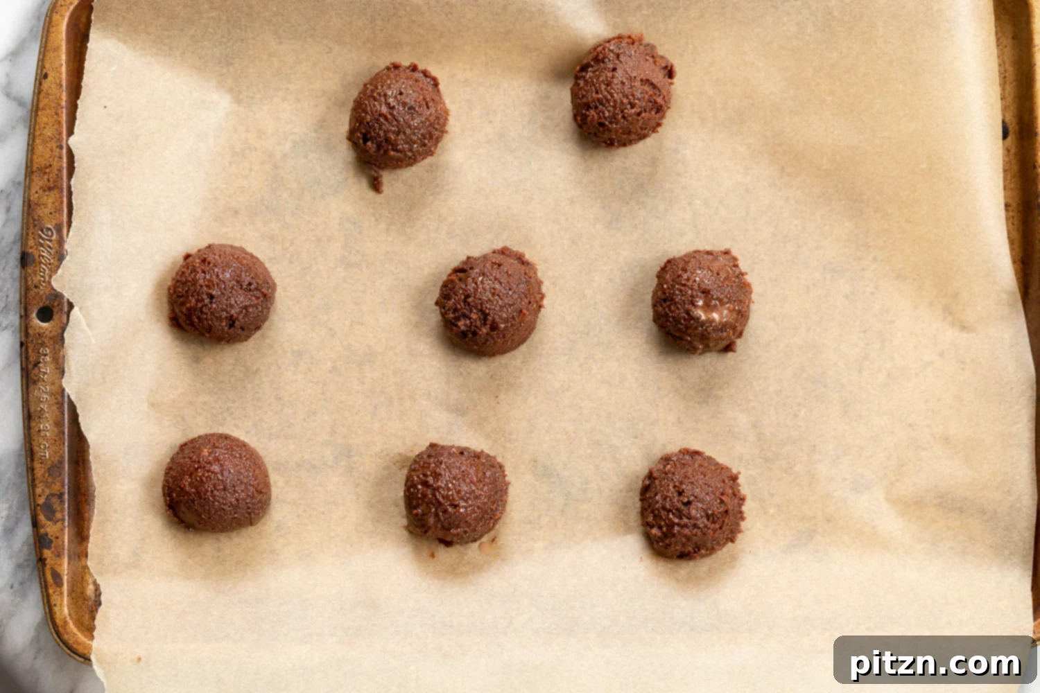 Scooped Vegan Brownie Cookie dough balls on a parchment-lined baking sheet, ready for the oven