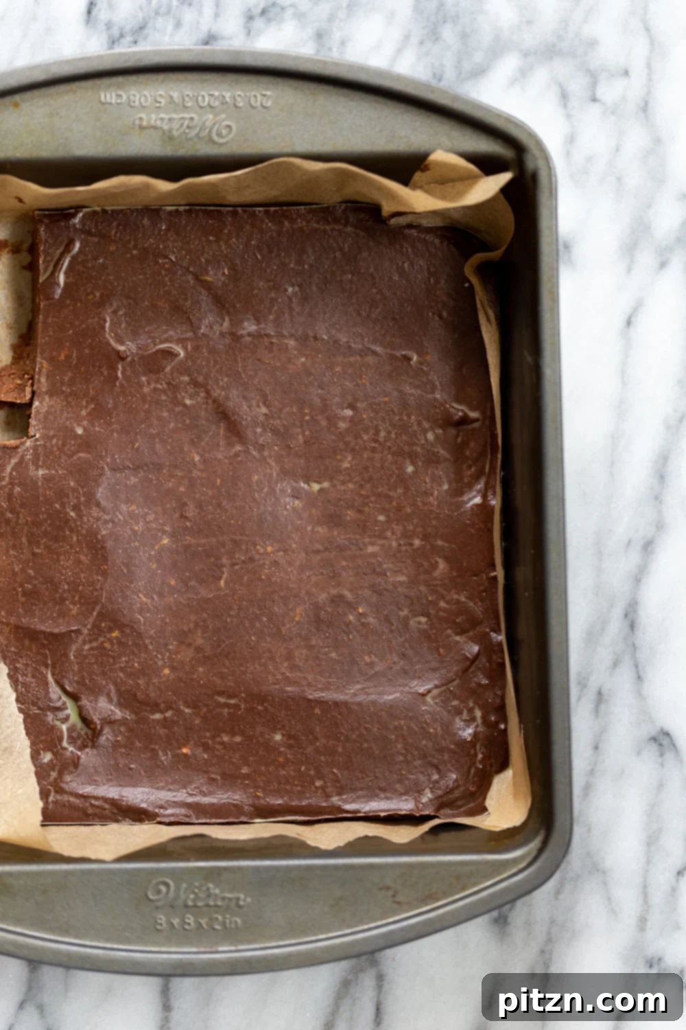 Easy 5-Ingredient Chocolate Avocado Freezer Fudge 3 Vegan Chocolate Avocado Freezer Fudge chilling in a parchment-lined brownie pan, showcasing its smooth texture before slicing.