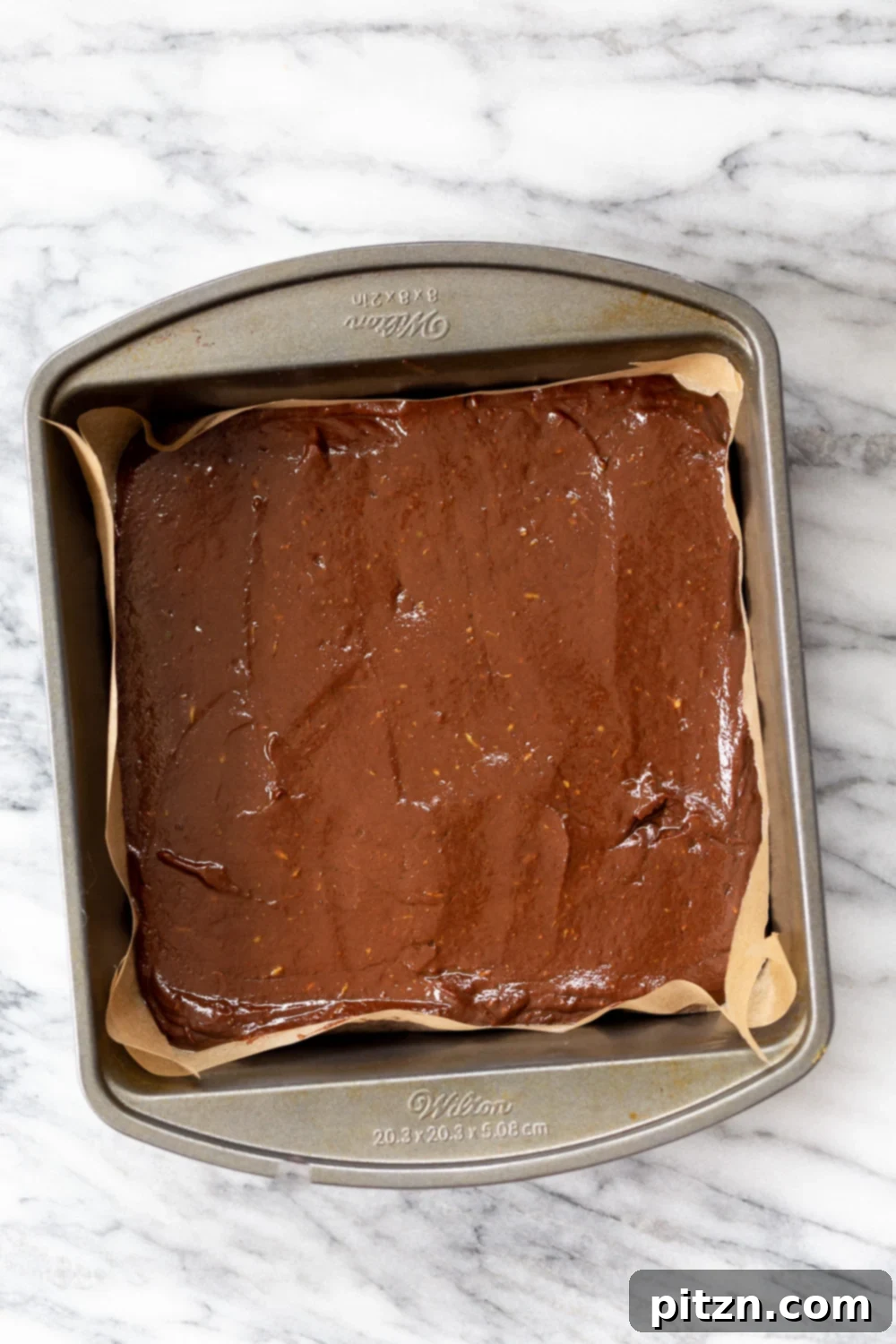 Easy 5-Ingredient Chocolate Avocado Freezer Fudge 9 A close-up shot of Vegan Chocolate Avocado Freezer Fudge bars in a parchment-lined brownie pan, showcasing their rich, dark color and smooth texture.
