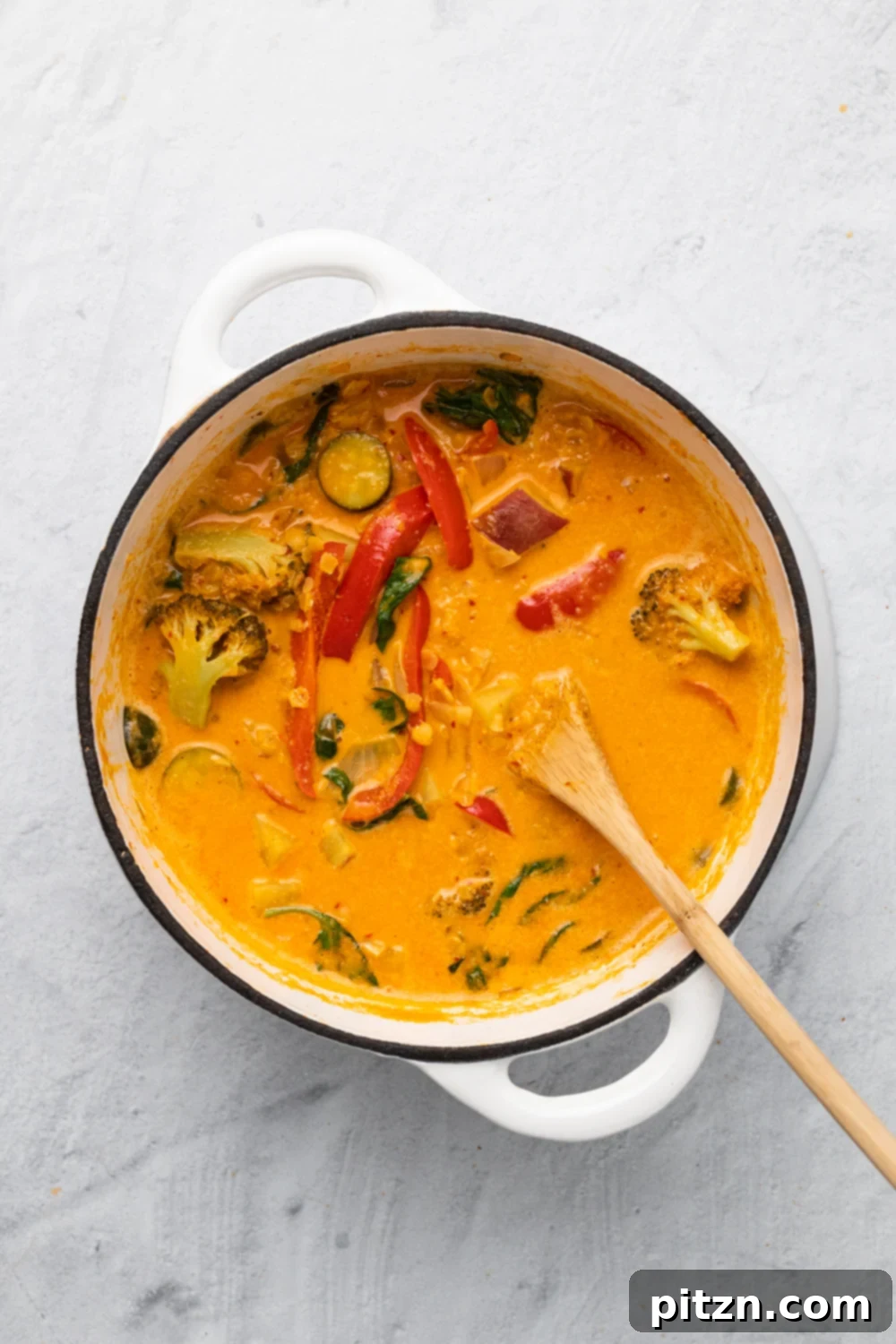 sweet potato curry overhead shot of a pot of vegan red lentil sweet potato curry in a white pot with a wooden spoon