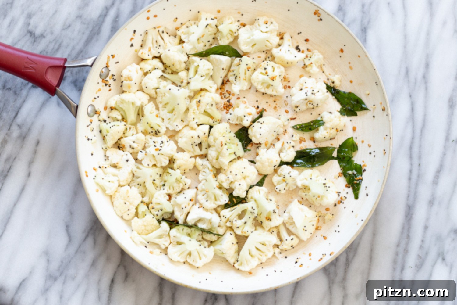 raw cauliflower florets being added to frying pan with Indian spices