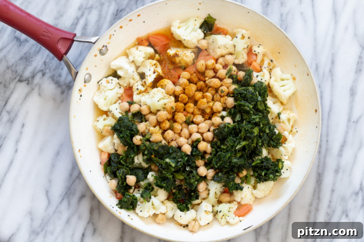 chickpeas and spinach being added to spices and par-cooked cauliflower to make Indian chickpea saute