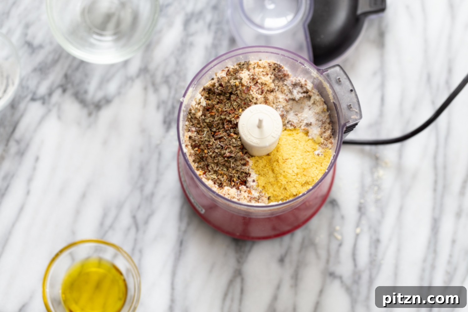 All dry ingredients for gluten-free vegan pizza bites, including herbs and spices, are combined in a food processor, ready for the final pulse. This step ensures even distribution of flavors in the savory snack balls.