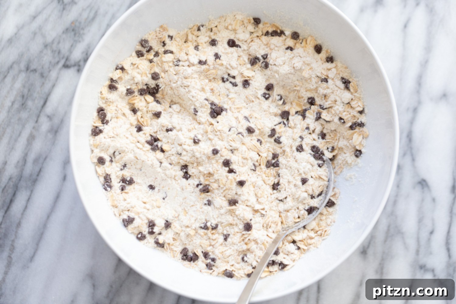 dry ingredients for vegan oatmeal chocolate chip waffles being stirred in a white bowl