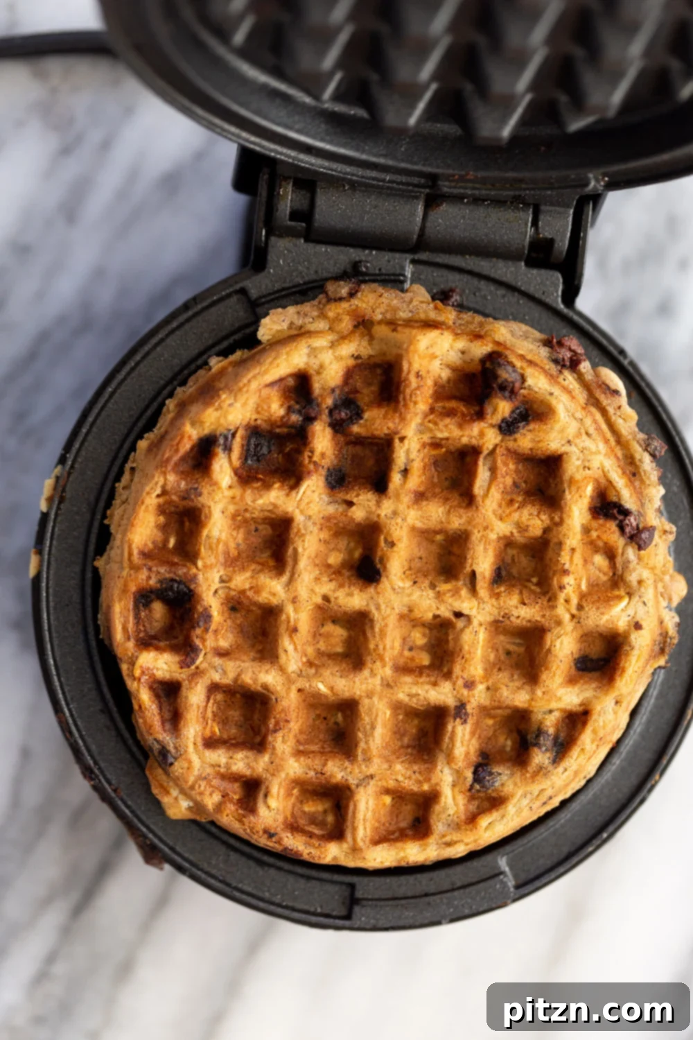 a vegan oatmeal chocolate chip waffle being baked in a black iron waffle maker 