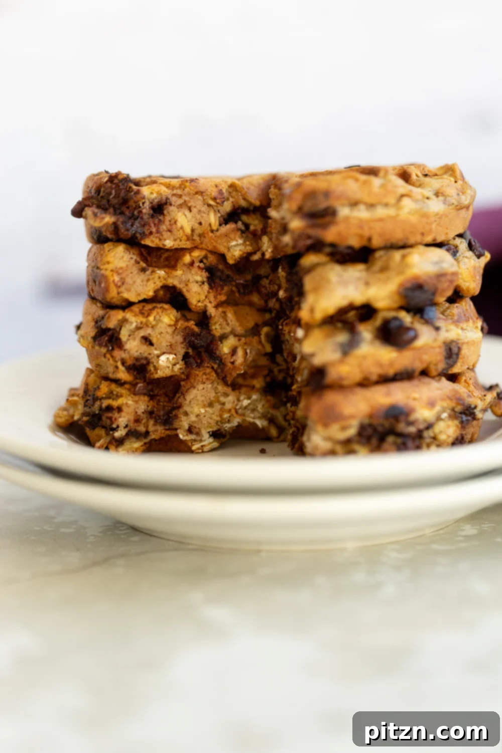 side view of a stack of crispy vegan oatmeal chocolate chip waffles on a white plate