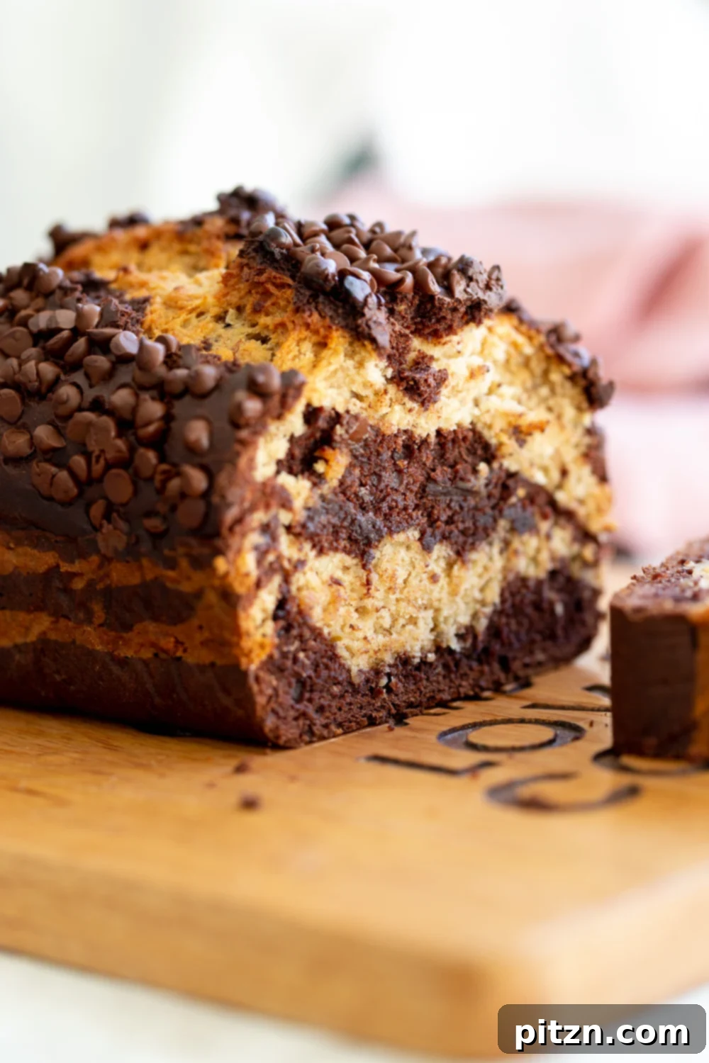 A perfectly sliced loaf of marbled vegan chocolate banana bread, topped with melted chocolate chips, resting on a rustic cutting board.