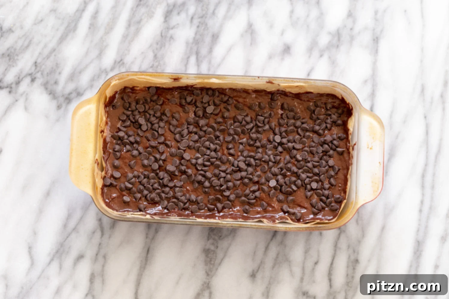 Close-up shot of the raw vegan chocolate banana bread batter in a loaf pan, beautifully topped with a generous sprinkle of vegan chocolate chips before baking.