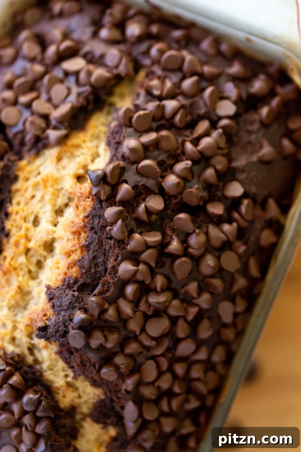 A beautiful close-up overhead shot of a freshly baked loaf of vegan chocolate banana bread, showcasing the golden crust and melted chocolate chips.