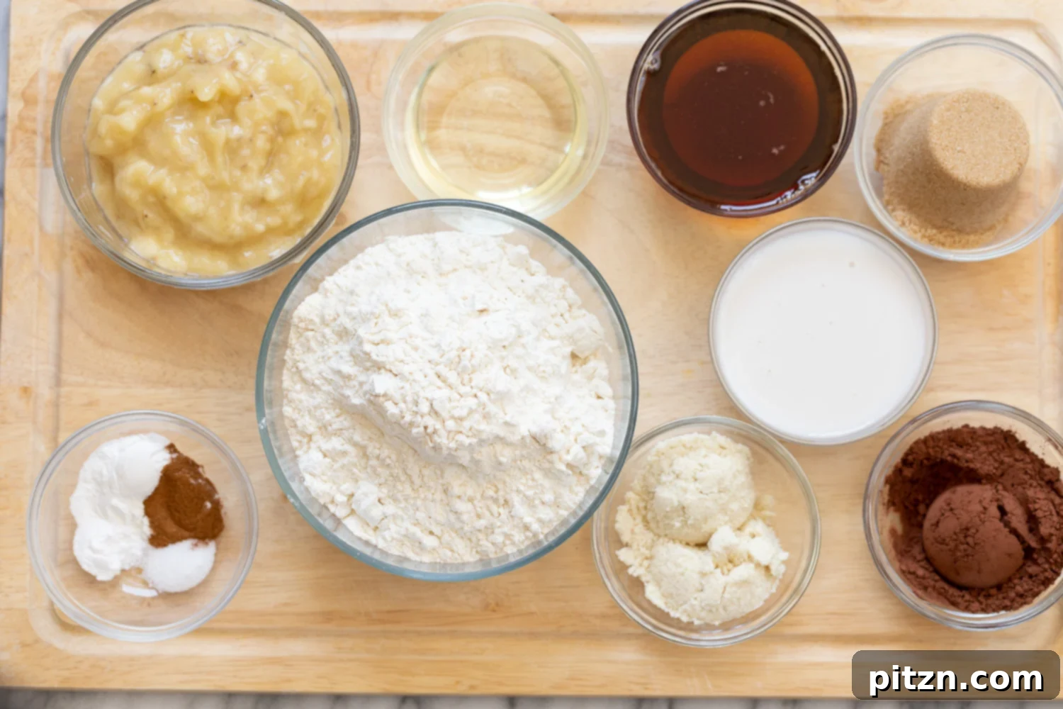 Overhead shot of all the carefully measured wet and dry ingredients laid out on a clean counter, ready for making vegan chocolate banana bread.