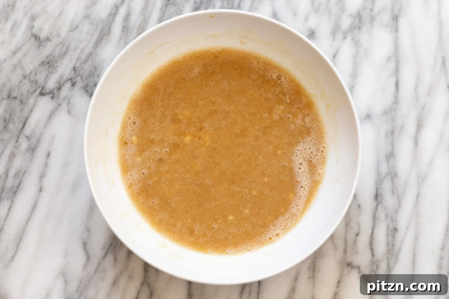 A bowl of wet ingredients for vegan banana bread being thoroughly mixed, showing a smooth, creamy texture ready for the dry components.