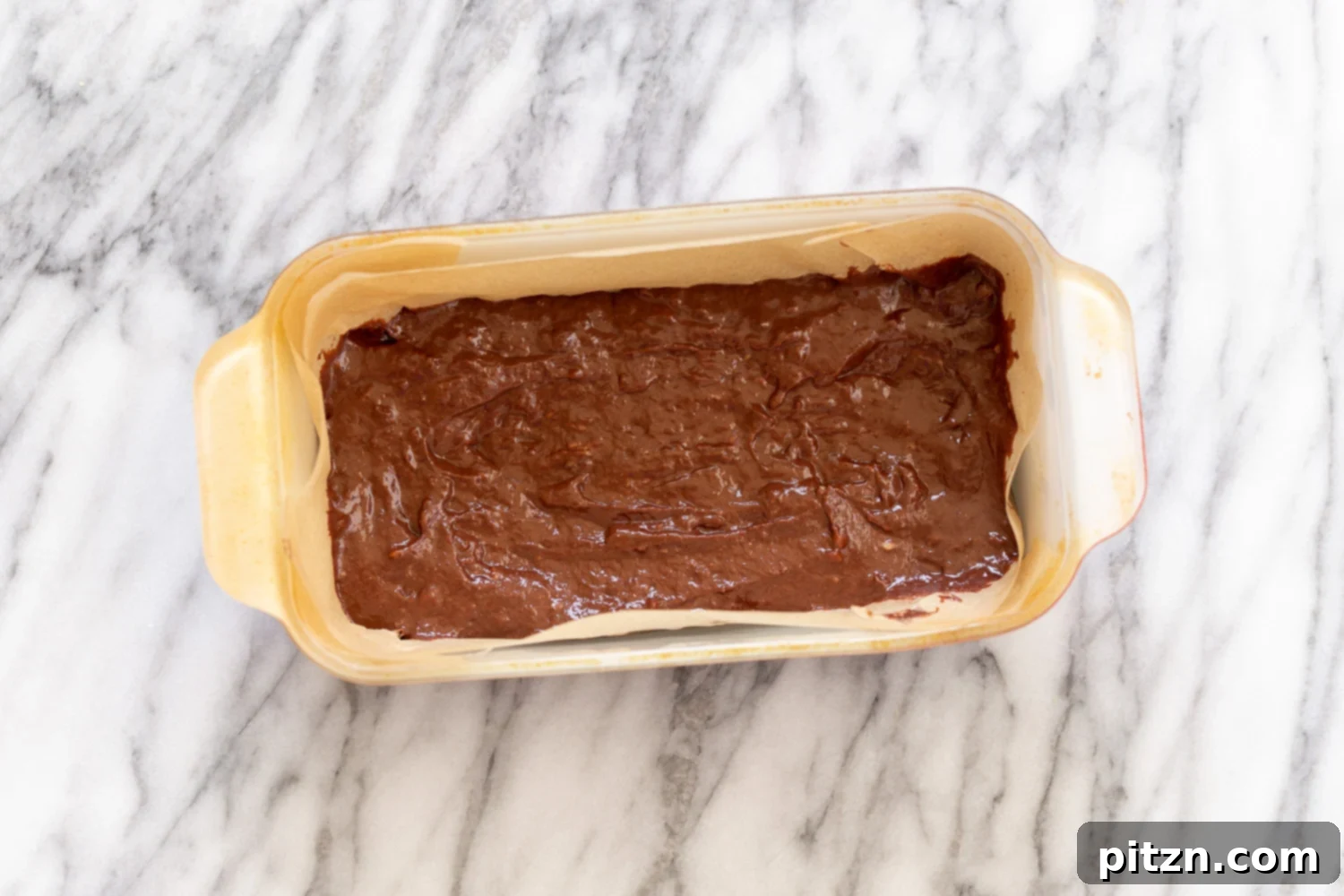 Overhead shot of the unbaked vegan chocolate banana bread batter, artfully swirled and ready to be baked in a parchment-lined loaf pan.