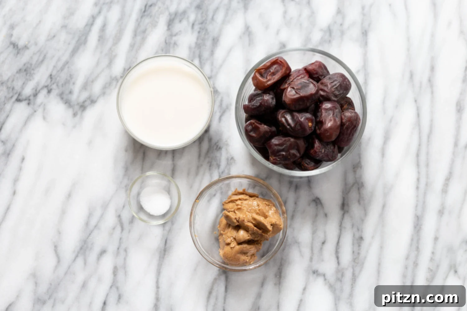 snickers recipe small glass dishes with plant based milk, dates, nut butter and salt on a kitchen counter