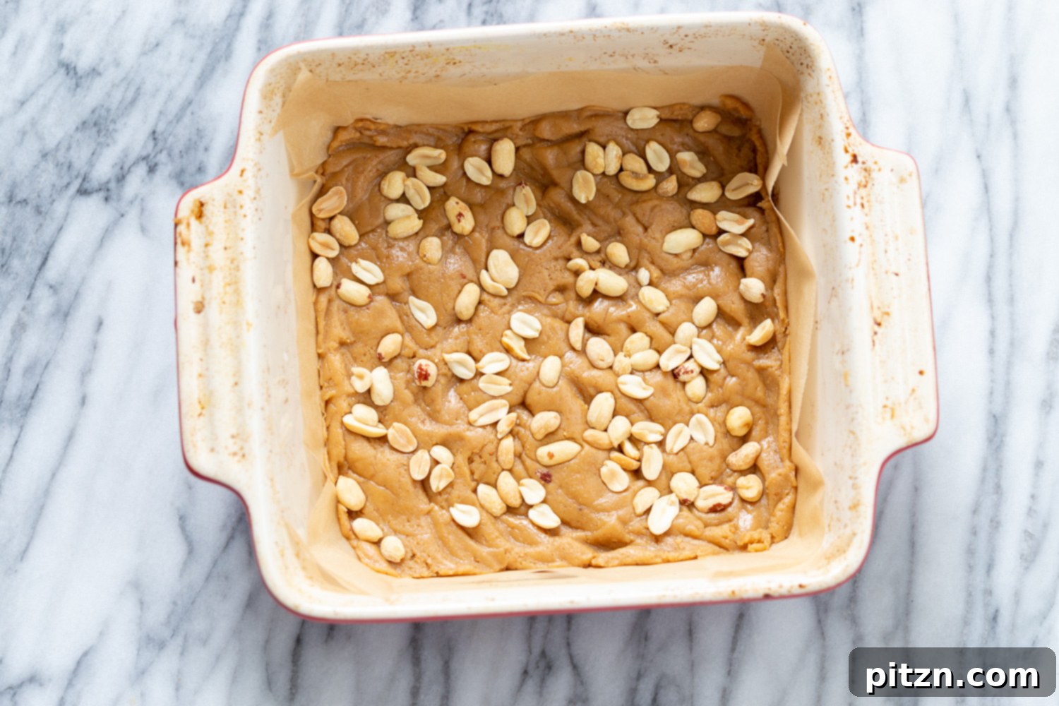 snickers bars recipe peanuts being sprinkled on cookie base to make vegan snack bars