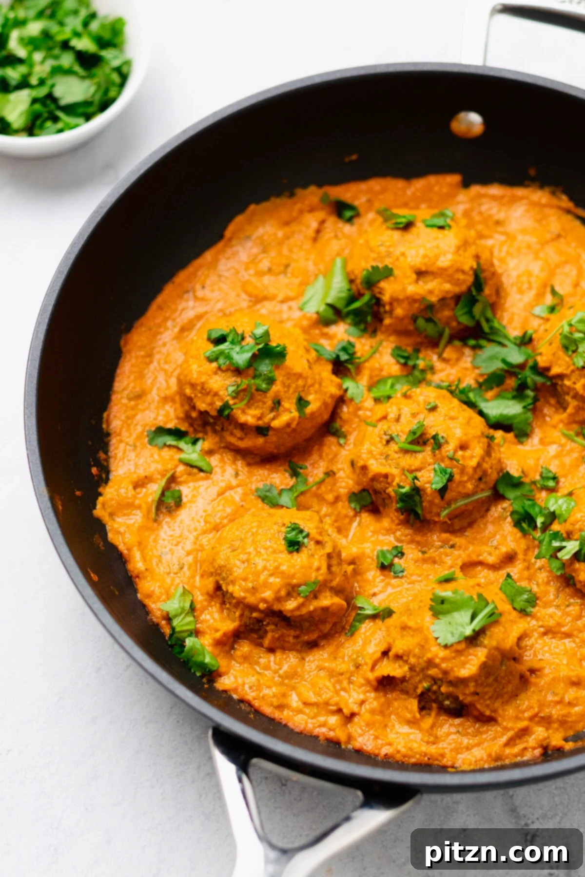 vegan malai kofta side view of a skillet with vegan malai kofta sprinkled with cilantro