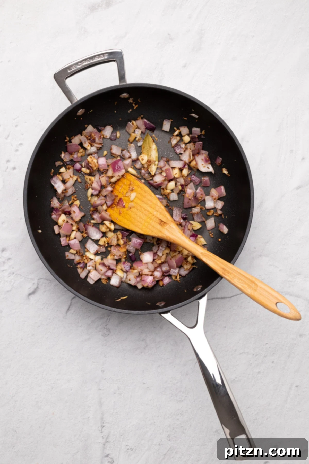 vegan malai kofta onions being stir-fried in a black skillet with spices to make malai kofta gravy