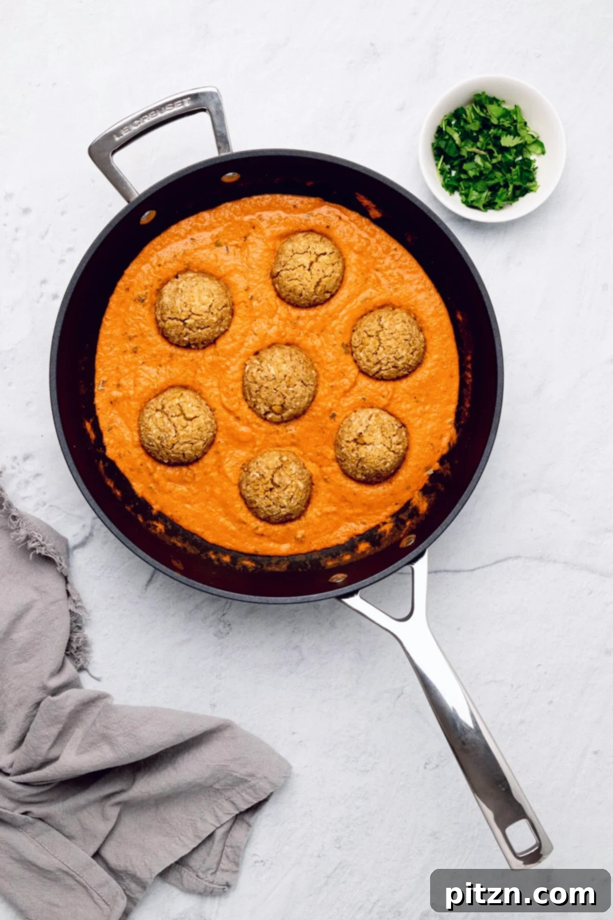 vegan malai kofta overhead shot of a skillet with vegan kofta in a dairy-free Indian gravy with chopped cilantro on the side
