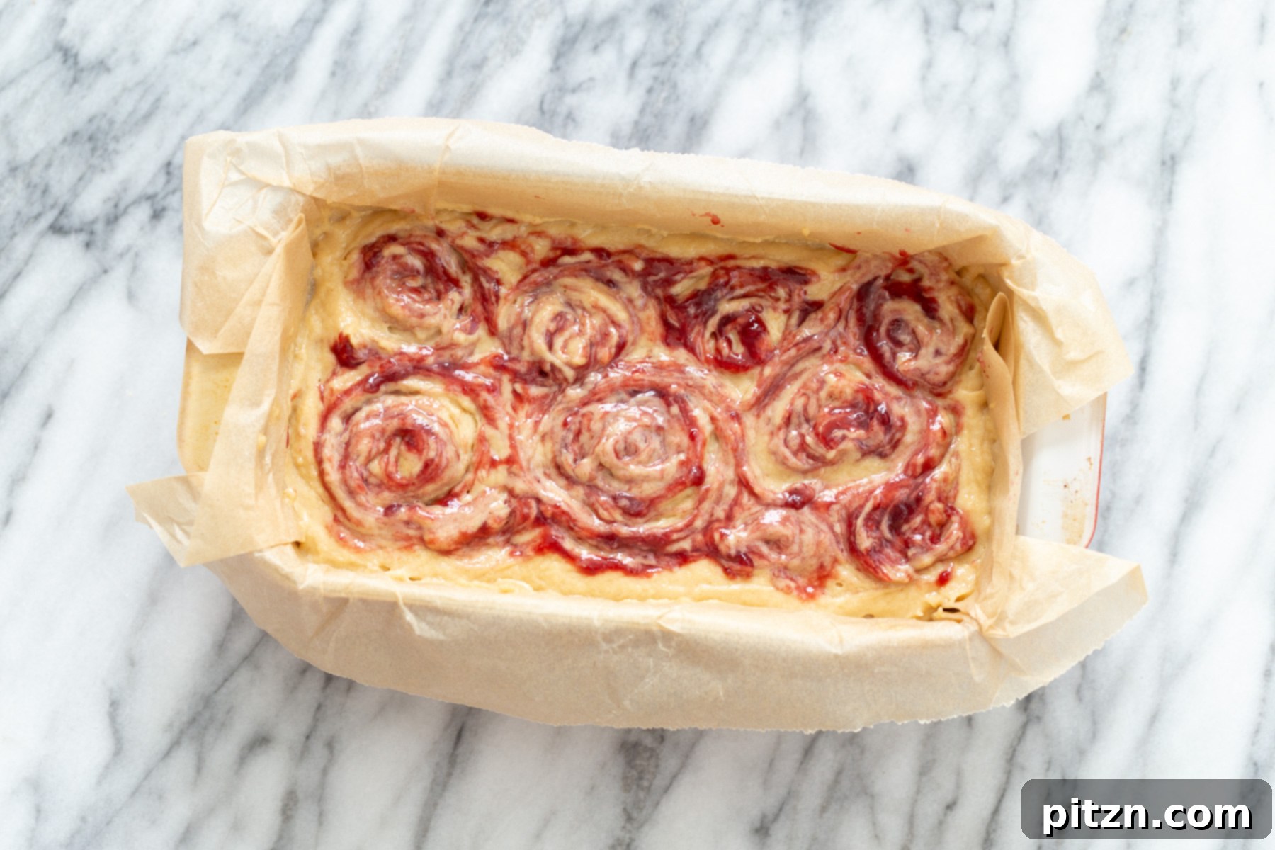 An unbaked vegan peanut butter and jelly cake in a loaf pan, with visible jam swirls, perfectly poised and ready to be put into the oven.