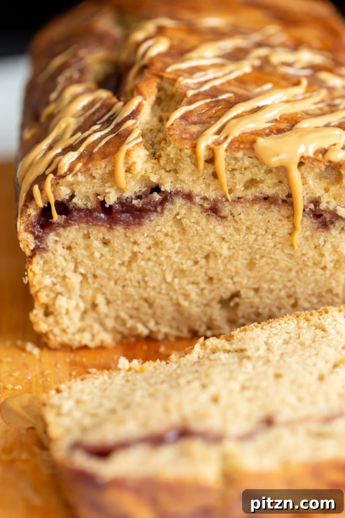 A close-up shot of a sliced vegan peanut butter and jelly loaf cake, showcasing the beautiful, distinct swirls of raspberry jam within its moist, tender crumb.