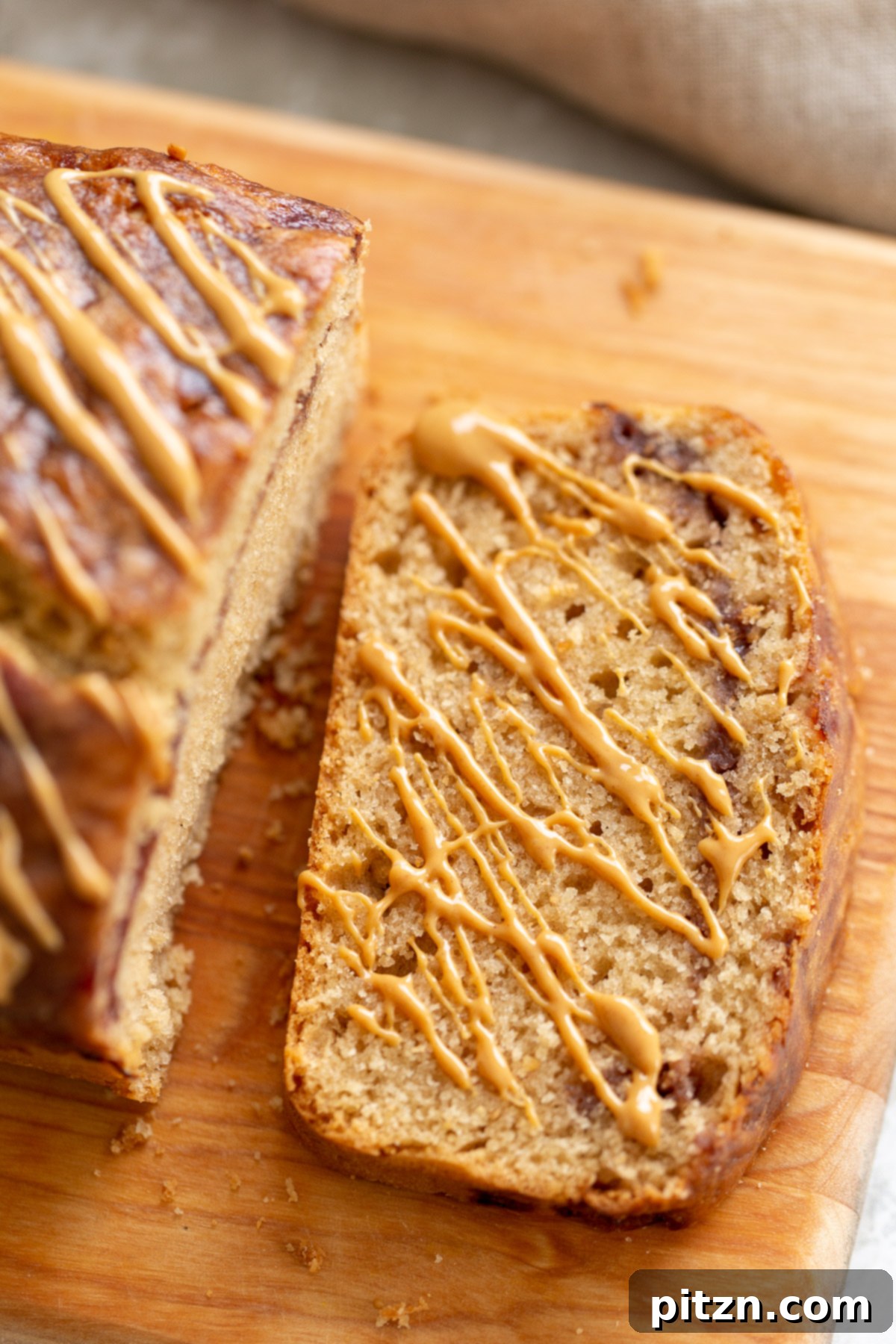 A single slice of vegan peanut butter and jelly loaf cake, generously drizzled with more creamy peanut butter, showcasing its appealing layers and rich texture.