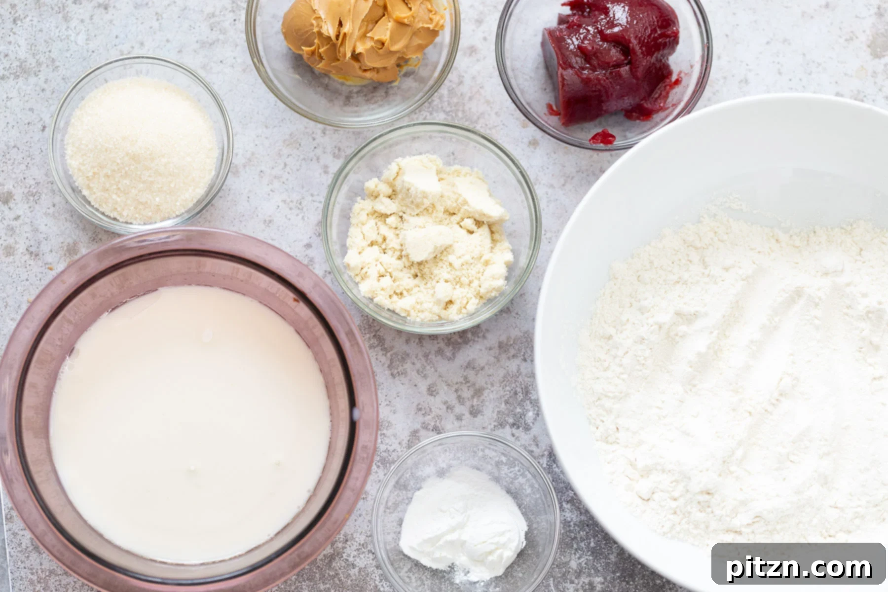 An overhead shot of all the ingredients meticulously laid out for the vegan peanut butter and jelly cake, including jars of jam, peanut butter, and measured flours.