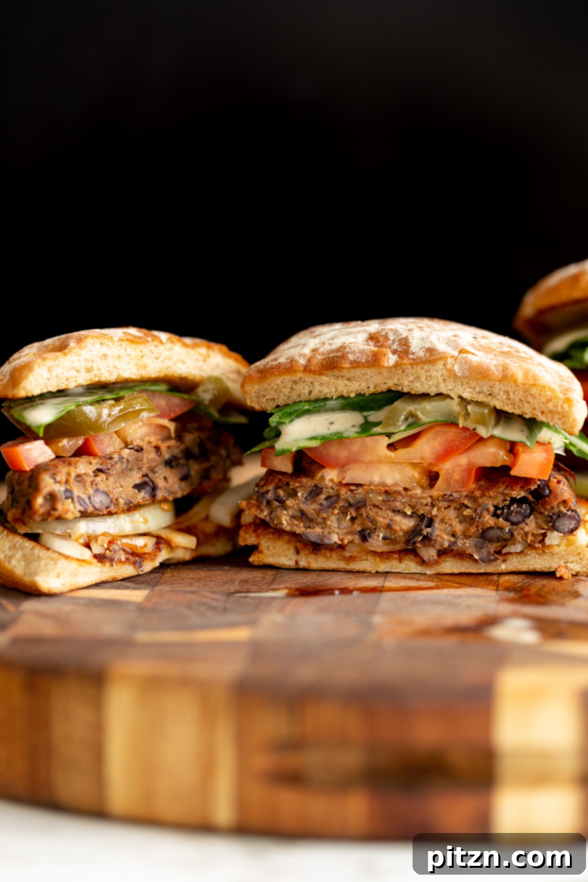 Halved Quinoa Black Bean Burger A halved vegan black bean quinoa burger showcasing its hearty interior, adorned with fresh tomato slices and a delicate drizzle of ranch sauce.