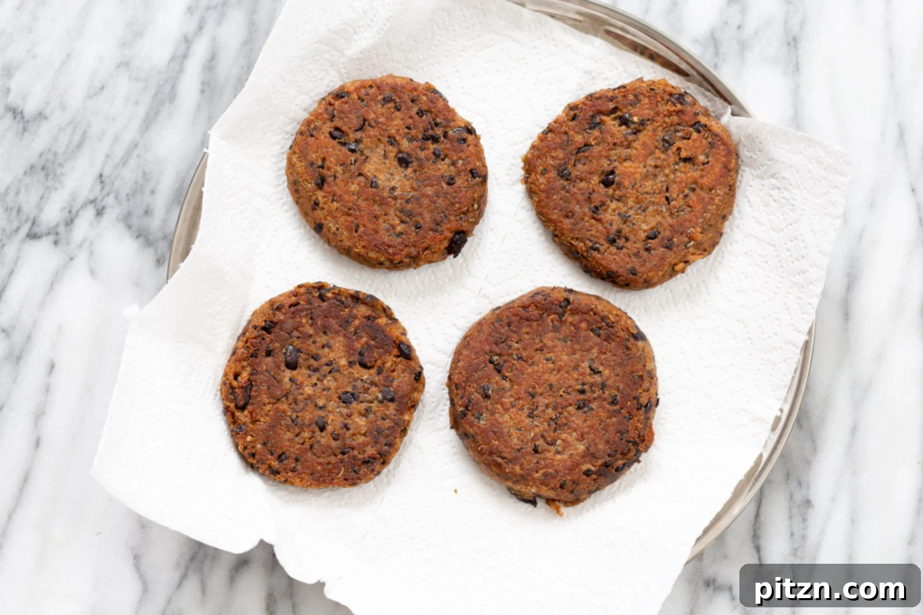 Pan-fried Quinoa Burgers A plate featuring perfectly pan-fried black bean quinoa burger patties, resting on paper towels to absorb any excess oil, ready to be served.