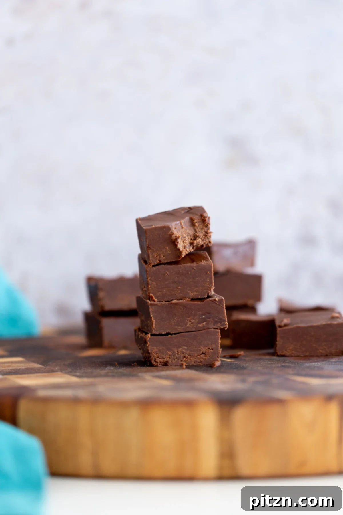 Side view of a stack of easy vegan chocolate fudge on a wooden board, showcasing its rich, dark color and smooth texture. Perfect for a quick, wholesome dessert or a festive treat.